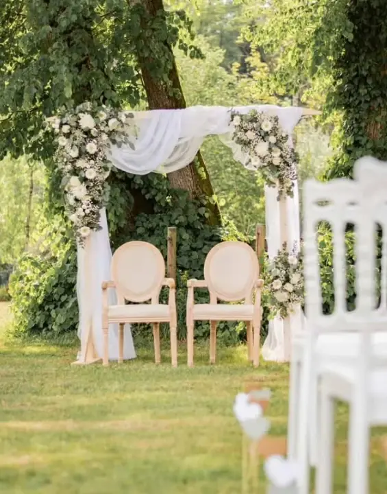 Arche de cérémonie laïque en plein air, drapée de voilage blanc et fleurie de roses blanches et de feuillages, par Mily Fleurs