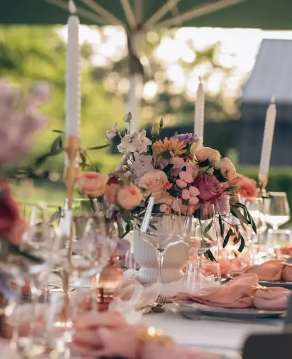Table de réception en plein air : centre de table de roses pêche, gerbera et lisianthus mauve entre de hautes bougies blanches, par Mily Fleurs